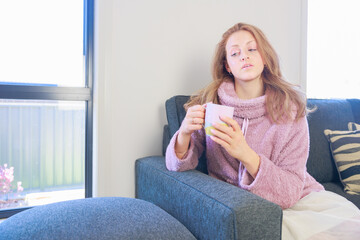 部屋でホットドリンクを飲む若い女性