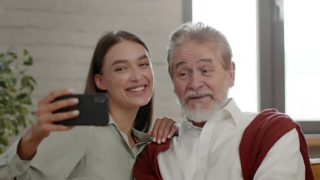 Happy family photo. Cute loving adult granddaughter taking selfie with senior grandfather, tracking shot, slow motion
