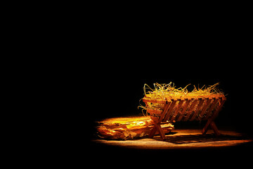 Manger with hay and old book on wooden table against dark background