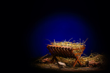 Manger with hay and stones on wooden table against dark blue background