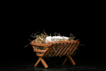 Manger with baby and hay on dark background