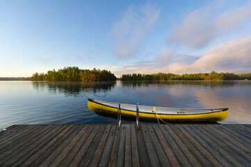 A yellow canoe is securely fastened to a rustic wooden dock nestled in the serene beauty of...