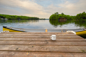 A yellow canoe secured to a wooden dock in Muskoka, Ontario, Canada, frames the serene backdrop of...