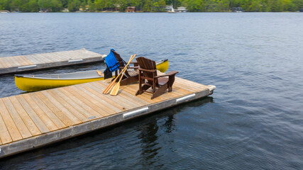 Two Adirondack chairs on a wooden dock face the serene blue waters of a Muskoka, Ontario lake....