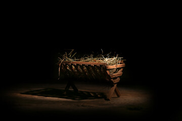 Manger with hay on wooden table against dark background