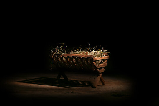 Manger with hay on wooden table against dark background