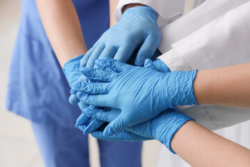 Doctors in medical gloves putting hands together at clinic, closeup
