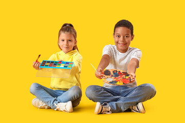 Cute little children with paints on yellow background
