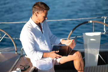 Successful mature man with a laptop working on a yacht