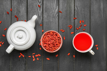 Bowl with red dried goji berries and cup of hot tea on black wooden background