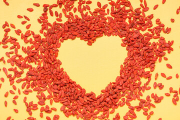 Heart made of red dried goji berries on yellow background