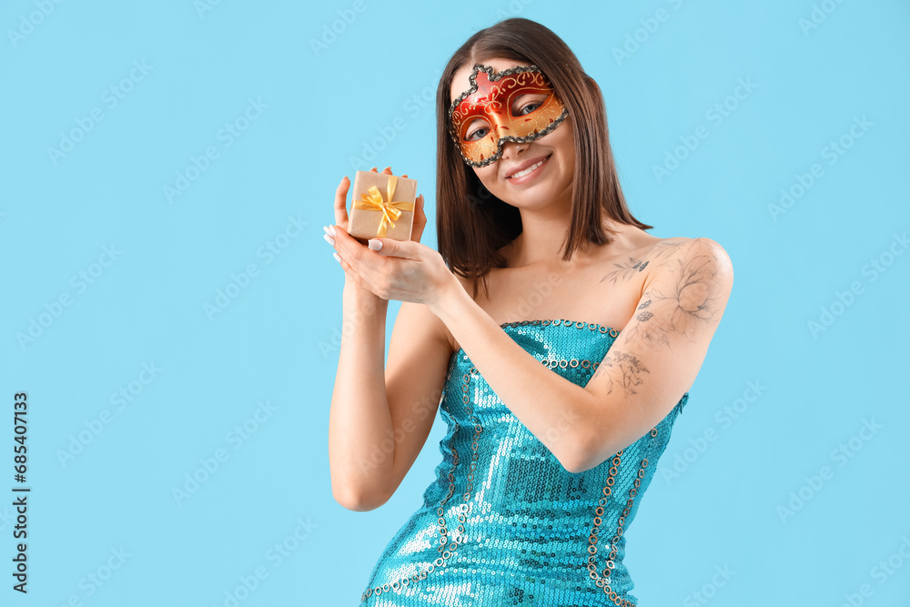 Sticker beautiful young woman in carnival mask with gift box on blue background