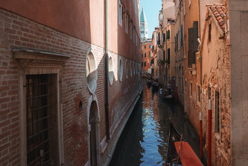 Fototapeta na wymiar Scenic view of a narrow canal in Venice, Italy, surrounded by traditional reddish-brown buildings. Clear and sunny weather creates a peaceful and timeless atmosphere.
