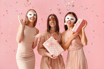 Beautiful young women in carnival masks with gift boxes on pink background