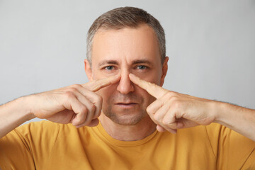 Ill mature man pointing at nose on grey background