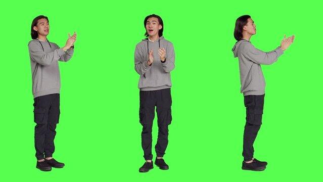 Asian happy guy applauding a person, clapping hands to show his congratulations and cheering for someone over full body greenscreen. Young man feeling optimistic and cheerful, standing ovation.