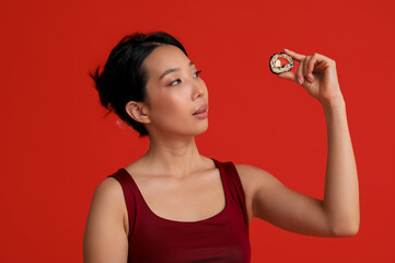 Beautiful young Asian woman with tasty maki roll on red background © Pixel-Shot