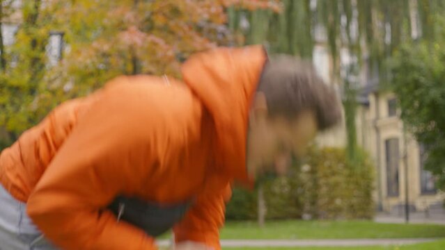 Young modern man with an orange jacket drops his modern smartphone in call on the asphalt on the street with, Side View Slow-Motion 4K UHD B-Roll footage