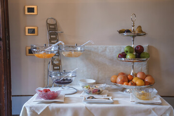 A side angle view of a buffet table with a variety of neatly arranged fruits on a white tablecloth, creating an elegant and sophisticated atmosphere. Apples, oranges, pears.