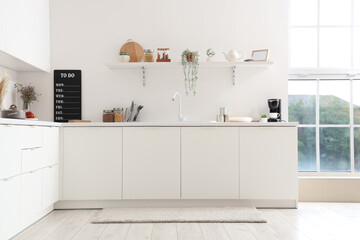 Interior of light kitchen with white counters, shelf, sink and utensils