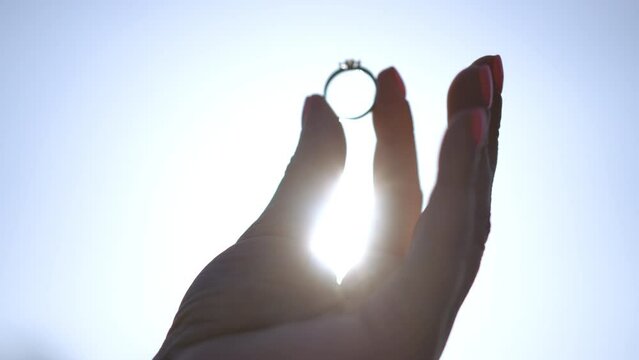 A woman looks at an engagement ring against the backdrop of dawn in a park in spring. Marriage proposal. The concept of marriage and family. Wedding ring in a woman's hands