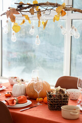Autumn table setting with pumpkins and pine cones in light dining room