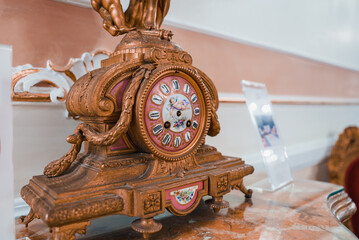 An elegant brown and gold ornate clock with a gilded face sits on a marble tabletop in a...