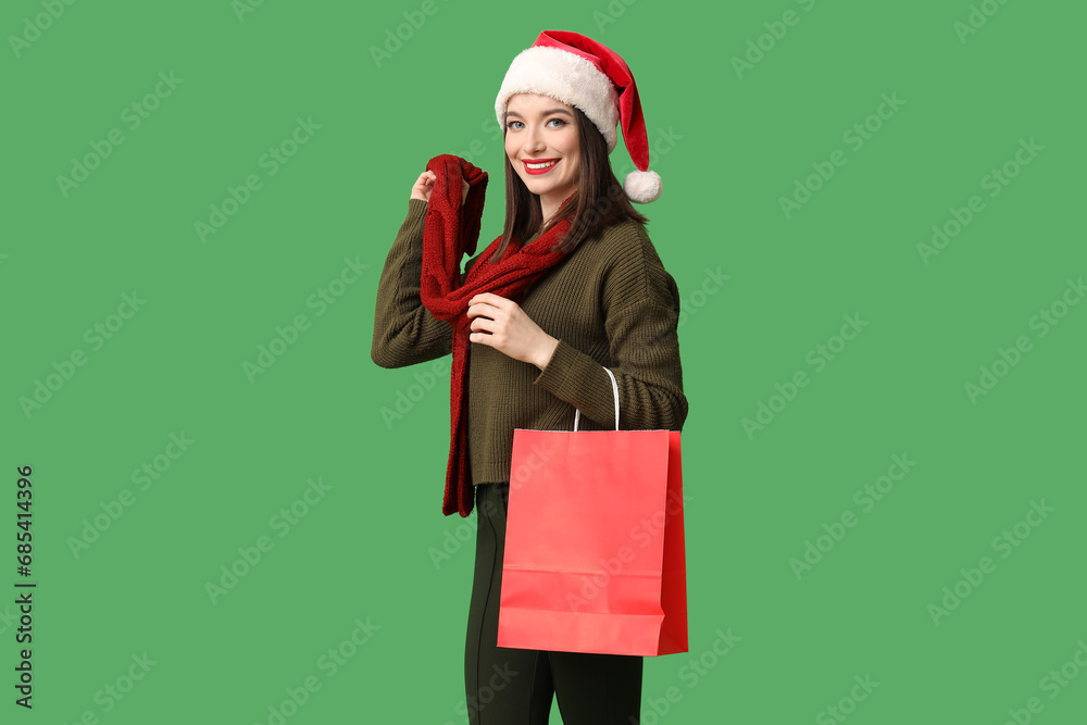 Sticker young woman in santa hat with shopping bag on green background