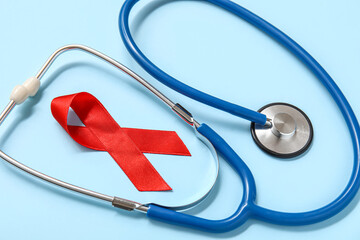 Red ribbon with stethoscope on blue background, closeup. AIDS Day concept