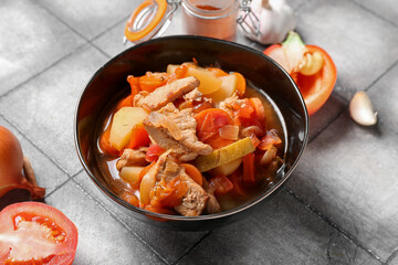 Bowl with delicious beef stew and different ingredients on grey tile background