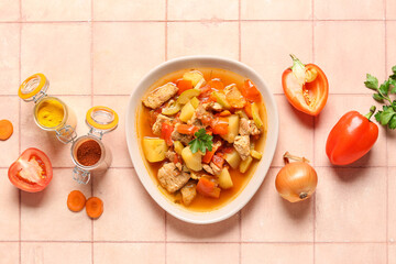 Bowl with delicious beef stew and different ingredients on pink tile background