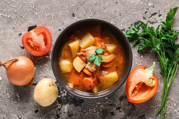 Black bowl with delicious beef stew and ingredients on grey background