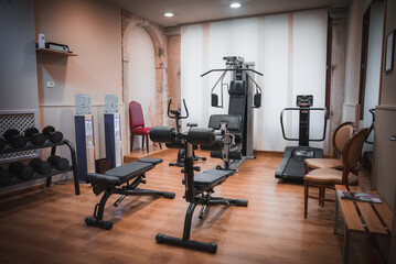 Modern gym room with exercise equipment including a rowing machine, captured from a side angle. No flooring or windows are visible. - obrazy, fototapety, plakaty