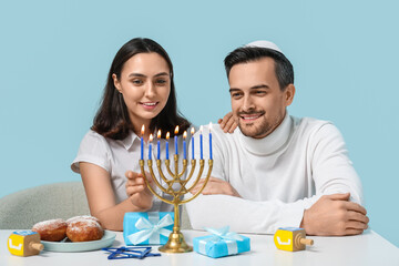 Fototapeta na wymiar Lovely couple sitting at table with menorah and Hanukkah decorations on blue background