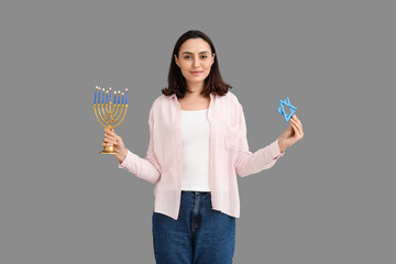 Pretty young woman with menorah and David star on grey background. Hanukkah celebration