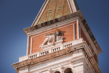 A majestic clock tower with a lion statue on top, set against a clear sky. The architectural style and location are unknown.