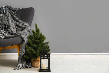 Modern armchair with blanket, Christmas tree and lantern near grey wall