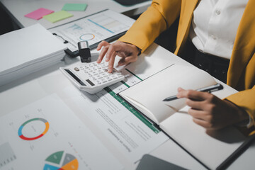 Female accountant working about financial with calculator at her office, Savings, Finances and economy concept, Beautiful Asian businesswoman analyzes charts using laptop calculator at the office.