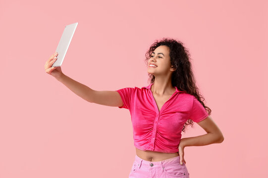Young African-American woman taking selfie on pink background