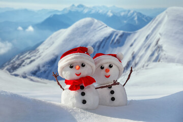View of a couple of snowmen in a santa hats on their heads against the backdrop of snowy mountains....