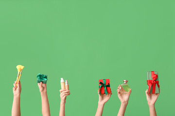 Female hands with different cosmetic products and gifts on green background