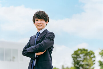 青空とオフィスの前に立つ若いアジア人ビジネスマン
