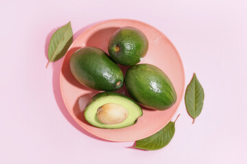 Plate with fresh ripe avocados and leaves on pink background