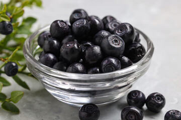 Ripe bilberries in bowl on light marble table, closeup