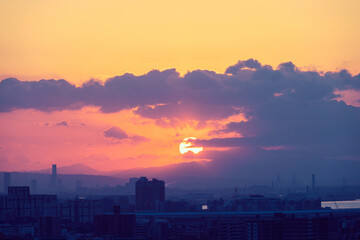 都市の夜明け。神戸市の高台から大阪湾と大阪南港から朝日が昇る。雲の隙間から天使の梯子。