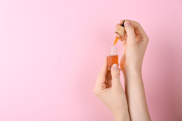 Woman holding bottle of essential oil on pink background, closeup. Space for text