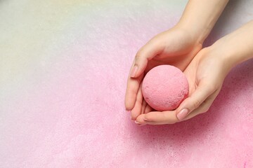 Woman holding bath bomb over water with foam, top view. Space for text