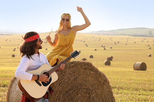 Beautiful hippie woman listening to her friend playing guitar in field, space for text