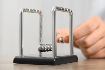 Man playing with Newton's cradle at table against light background, closeup. Physics law of energy...
