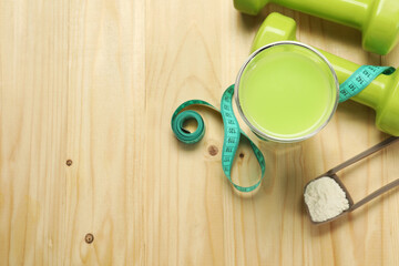 Tasty shake, dumbbells, measuring tape and powder on wooden table, flat lay with space for text. Weight loss